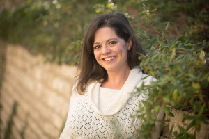 Photograph of poet Traci Brimhall, a smiling woman with dark hair, wearing a white sweater