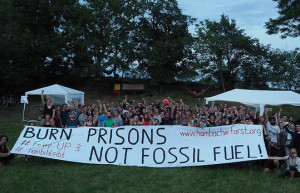 crowd on grass near trees with sign that reads "Burn Prisons not Fossil Fuels"